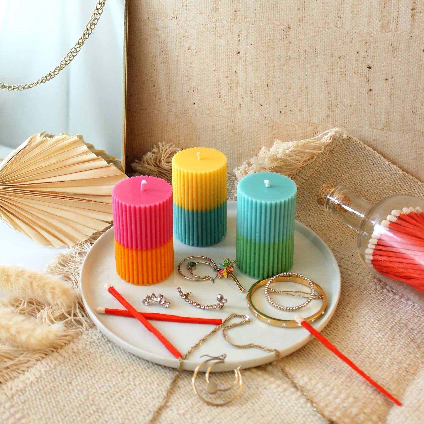 Image of three two tone candles on a dish with jewellery and matches around it showing an example of candle decoration ideas