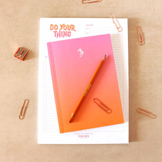 Planner book on a table with a notepad, pencils and paper clips