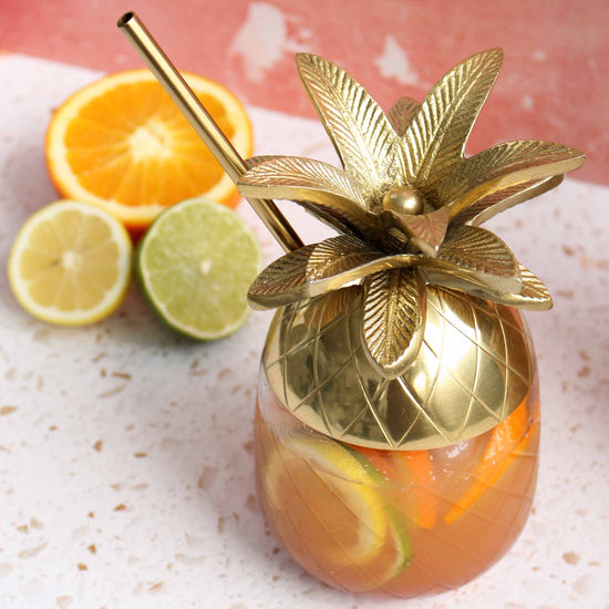Image of rum punch drink in a cup shaped like a pineapple with cut citrus fruits in the background