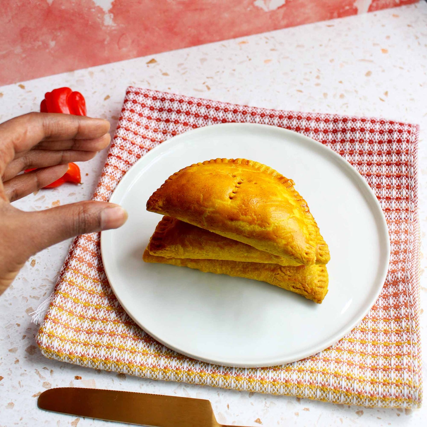 Image of a stack of Jamaican patties on a white plate and a hand reaching to take one