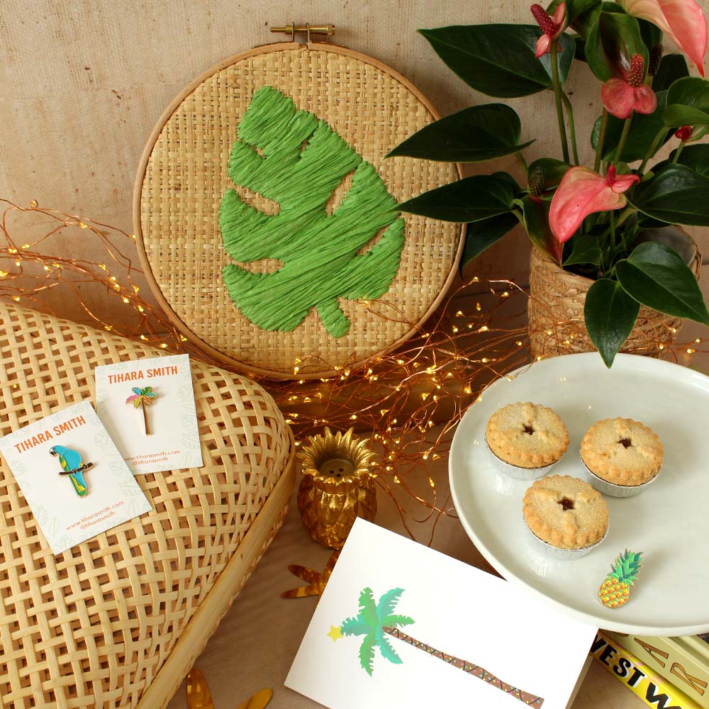 Image of monstera raffia embroidery hoop on a table next to a plant, Christmas card, enamel pins and mince pies.