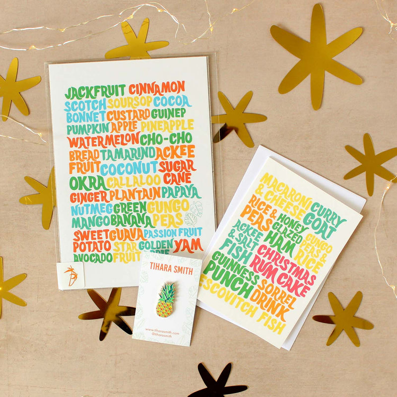 A Caribbean island food art print, Caribbean Christmas dinner greeting card and a pineapple pin on a beige surface.