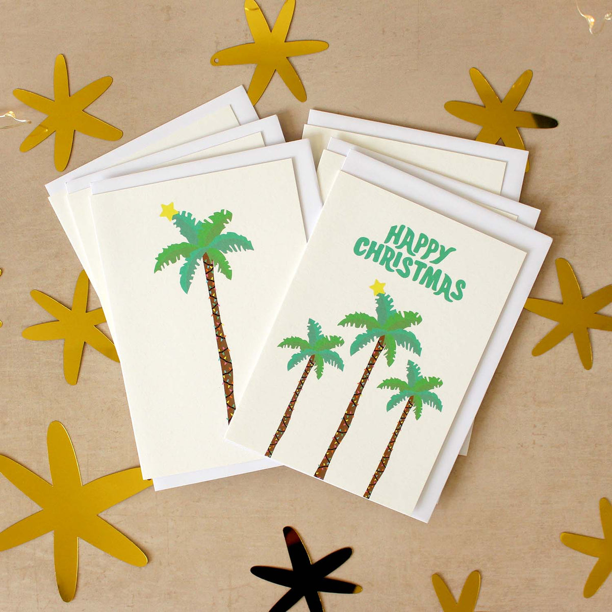 Stack of six palm tree Christmas cards on a beige surface with star cut outs around them.