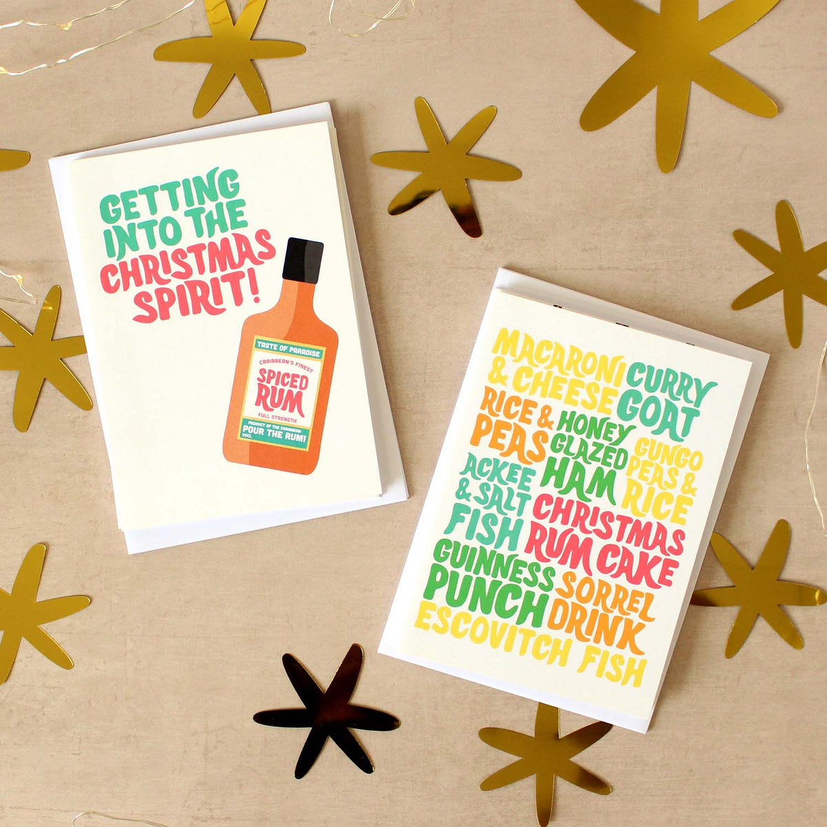 Stacks of Caribbean-inspired Christmas cards on a beige surface surrounded by gold star confetti.