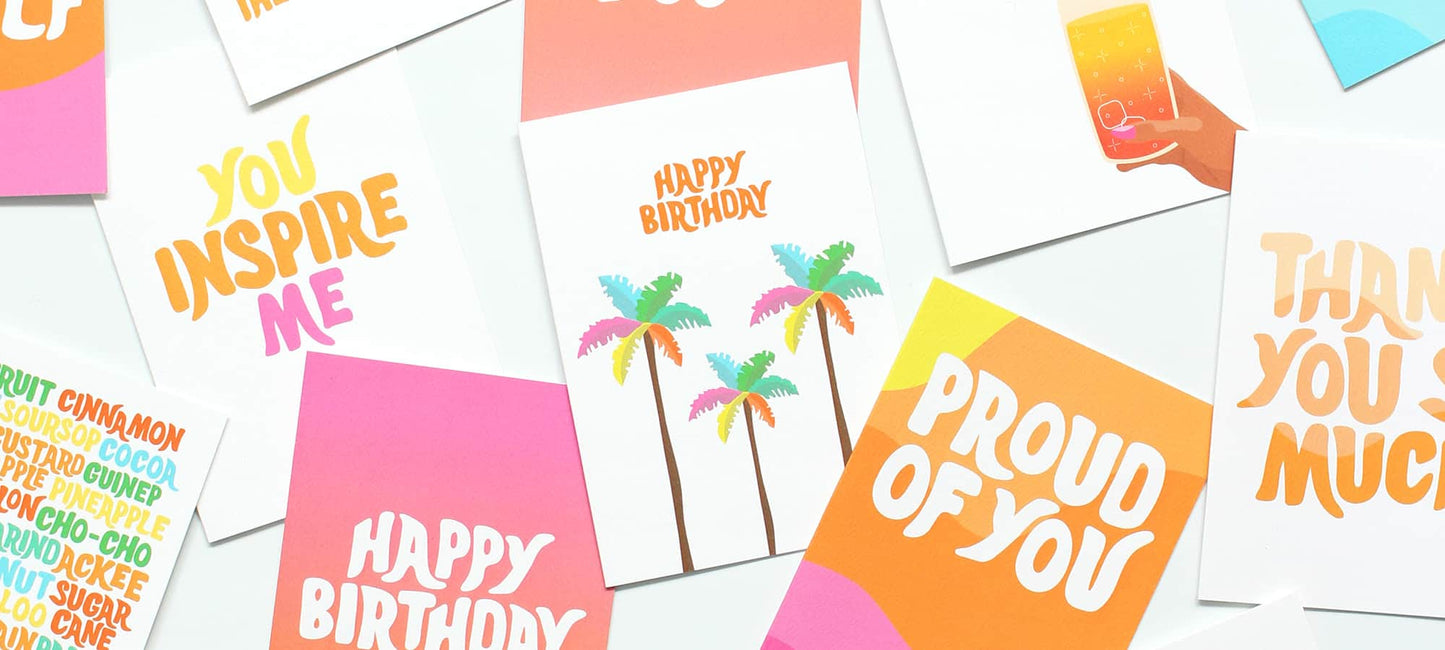 A flat-lay arrangement of various colourful greeting cards on a white background, featuring designs with palm trees, cocktail graphics, and birthday and thank-you messages.