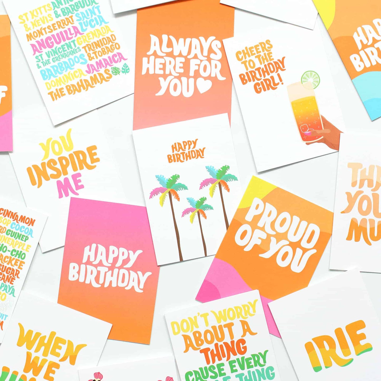 A flat-lay arrangement of various colourful greeting cards on a white background, featuring designs with palm trees, cocktail graphics, and birthday and thank-you messages.